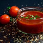 Jar of tomato sauce with two cherry tomatoes outside the jar