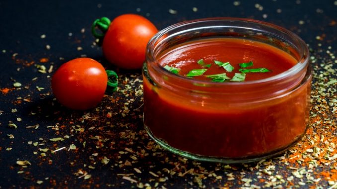 Jar of tomato sauce with two cherry tomatoes outside the jar